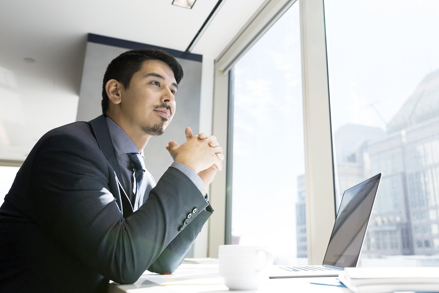 A businessman at laptop looking out urban office window