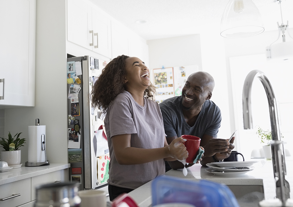 Father and teenage daughter laughing, doing dishes in kitchen