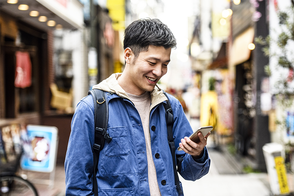 Cheerful young man looking at smartphone in street