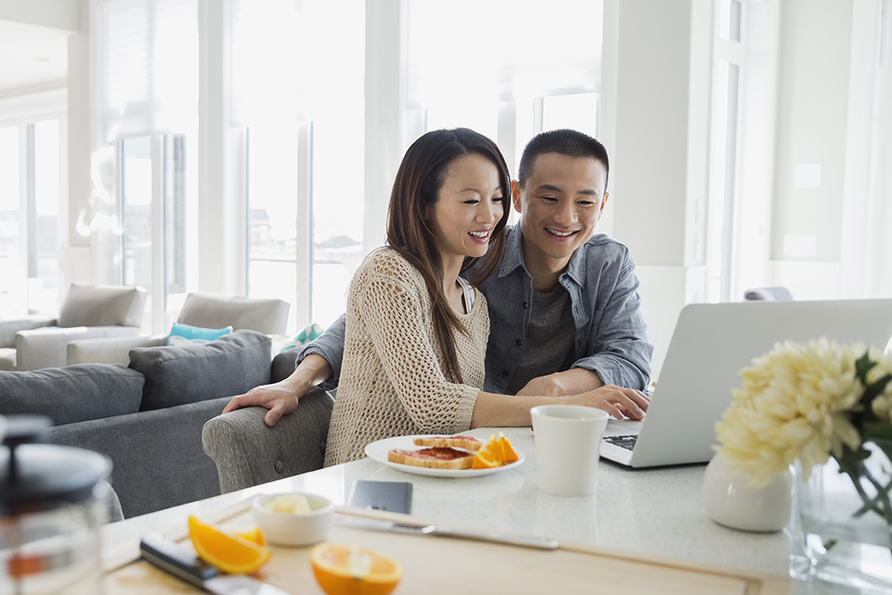 Couple at laptop in kitchen at breakfast