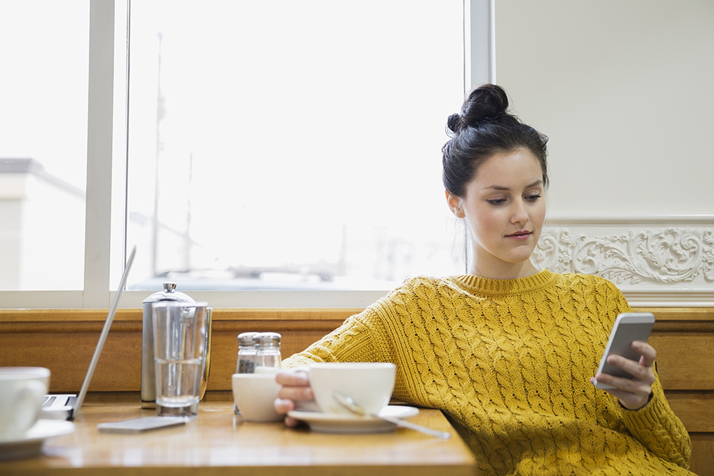 Woman texting and drinking cappuccino in cafe