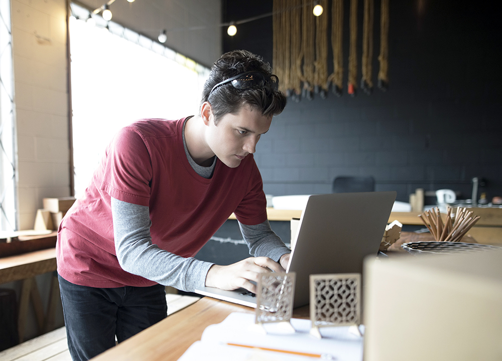 Focused male designer working at laptop in workshop