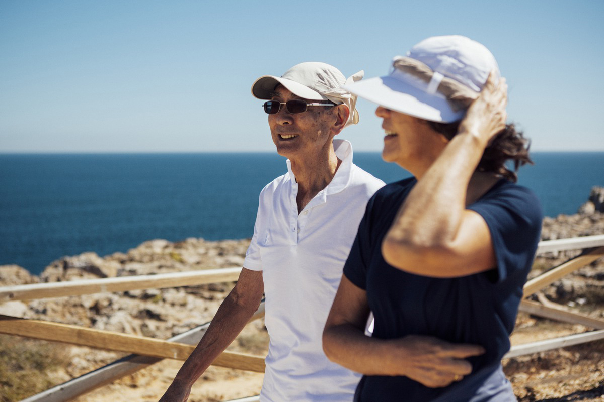 Smiling senior couple looking at sea while standing by railing against clear sky