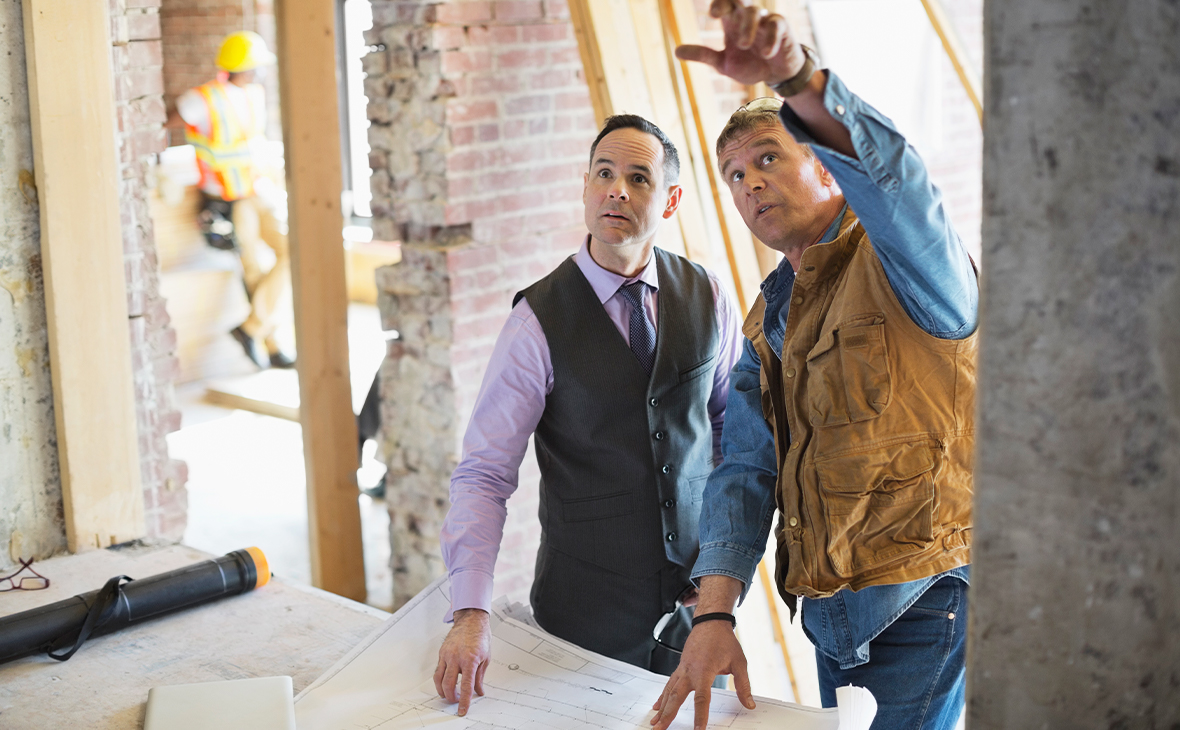 Male architect discussing blueprint with foreman at construction site.