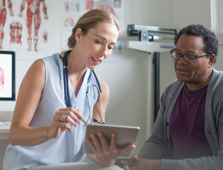 Female doctor with digital tablet talking with senior male patient in examination room