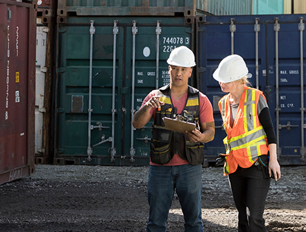 Workers inspecting empty shipping container in industrial container yard.