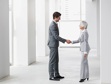 Businessman and businesswoman handshaking in empty office.