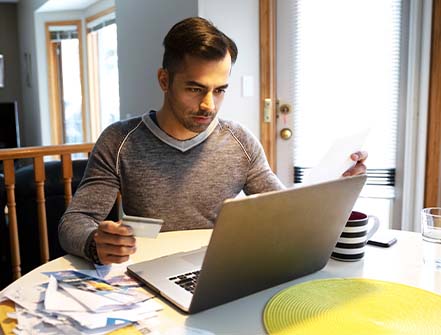 A man with credit card paying bills at laptop