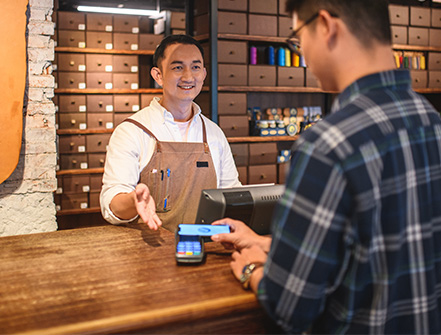 A merchant guides his client to use electronic payment method at his place of business.