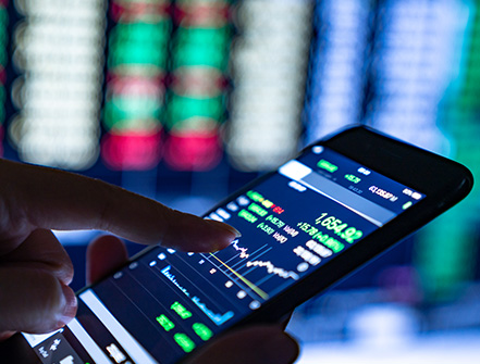 Una persona sostiene su teléfono celular y toca la pantalla que muestra sus opciones de inversión en una aplicación financiera.