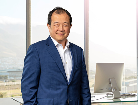 Chang M. Liu se para dentro de una sucursal de Cathay Bank con un traje azul oscuro y sonríe a la cámara.