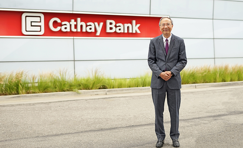 A bank executive in a suit standing in front of the Cathay Bank logo outside the corporate building.