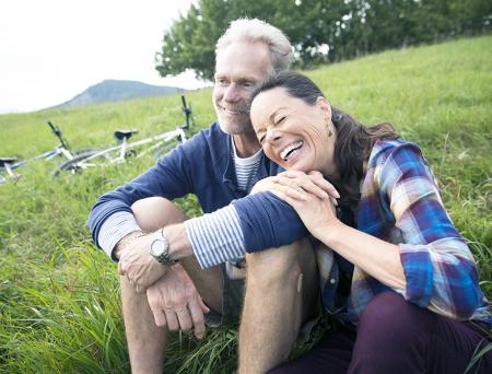 Laughing senior couple relaxing near mountain bikes in remote rural field