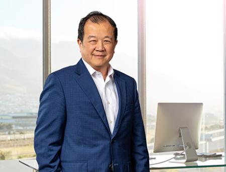 Chang M. Liu se para dentro de una sucursal de Cathay Bank con un traje azul oscuro y sonríe a la cámara.