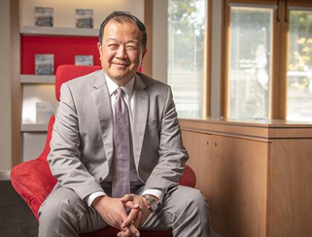 国泰银行总裁兼首席执行官在圣马力诺分行内拍摄专业照片，身穿棕褐色西装，白色领衬衫，系着玫瑰粉色领带。