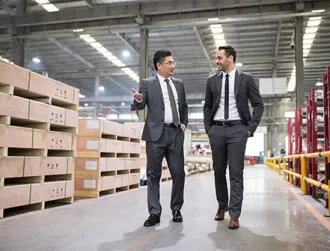 Two business men walk together through a warehouse to discuss cross-border financing.
