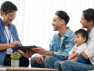 A life insurance policy manager shares a digital device with a family and their child while they sit on a couch in an office. 