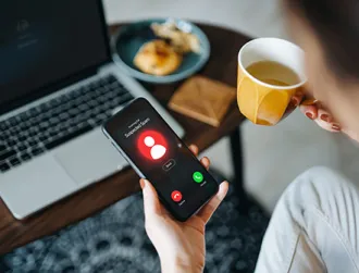 Over the shoulder view of young Asian woman receiving an incoming suspected call from unknown caller on her smartphone and rejecting the call at home. Device screen showing warning sign as detected by the network provider.