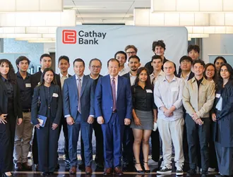 A large group of students and Cathay Bank representatives standing together in front of a Cathay Bank-branded backdrop. The group is dressed in business or business casual attire, posed for a formal group photo inside the corporate offices, with modern lighting and interior décor in the background.