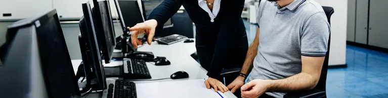 Two IT professionals in a big control room of a factory talking.