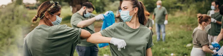 Group of volunteers with surgical masks cleaning nature together.