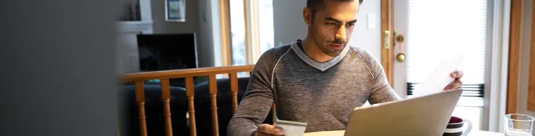 A man with credit card paying bills at laptop