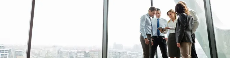 A group of office workers huddle around a digital tablet in a modern lobby.