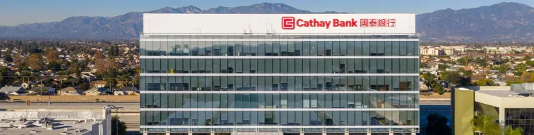 Cathay Bank’s corporate office building is pictured amongst the San Gabriel Valley mountains in the background and a Forbes logo is alongside it.