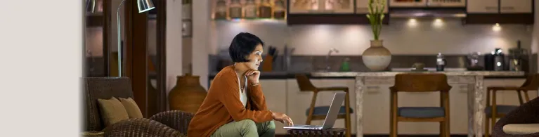 A woman with short black hair sits on a couch at home while trying to open an online banking account using her laptop.