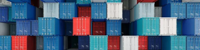 Blue, green, red, teal, and white shipping containers are lined up at an international port.