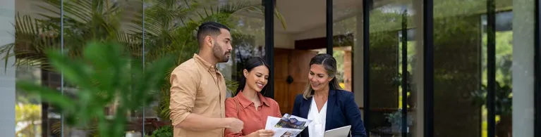A professional female real estate banker shares purchase options to a female and male couple interested in buying a home while standing in a patio.