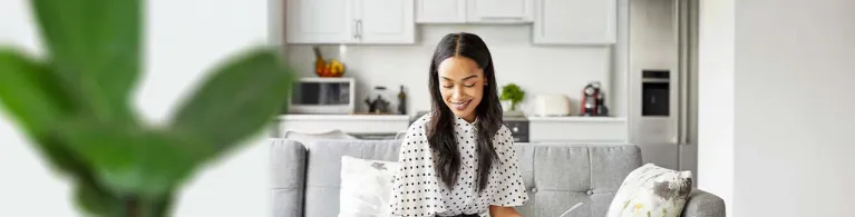 A young adult sits on her couch at home while planning for retirement on her laptop.