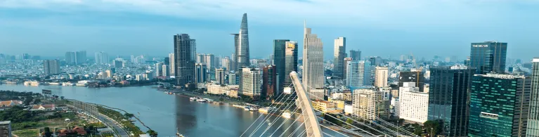 Panoramic view of a modern city skyline along a wide river, featuring numerous high-rise office and residential buildings of Ho Chi Minh City, Vietnam. 