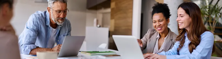 People working together at a table using laptops in a modern office setting, representing business online banking support.