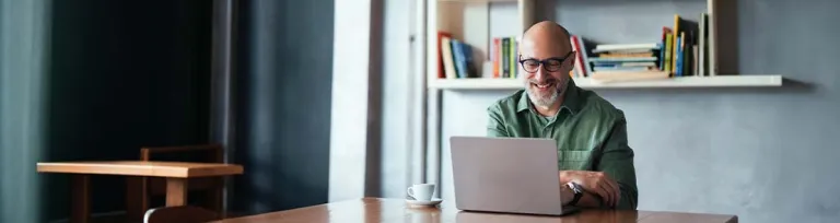 Smiling Man Working on Laptop in Modern Workspace with Bookshelves