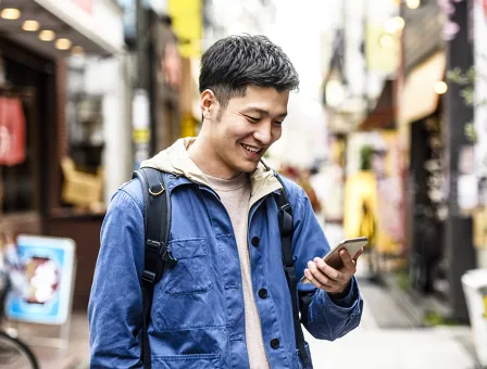 Cheerful young man looking at smartphone in street