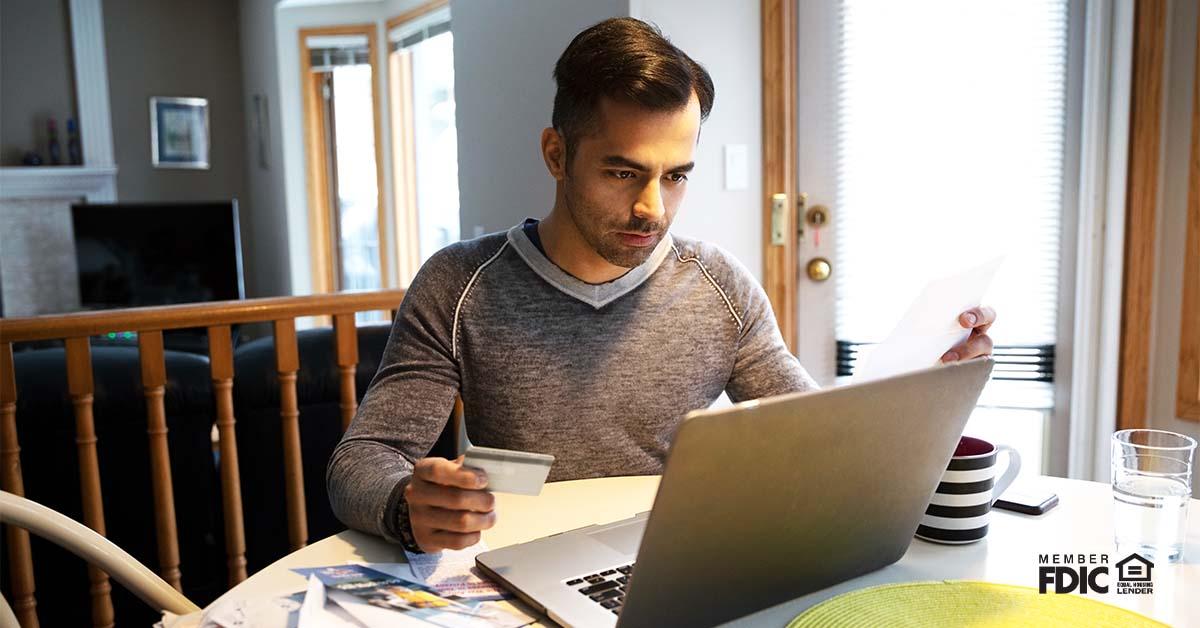 A man with credit card paying bills at laptop