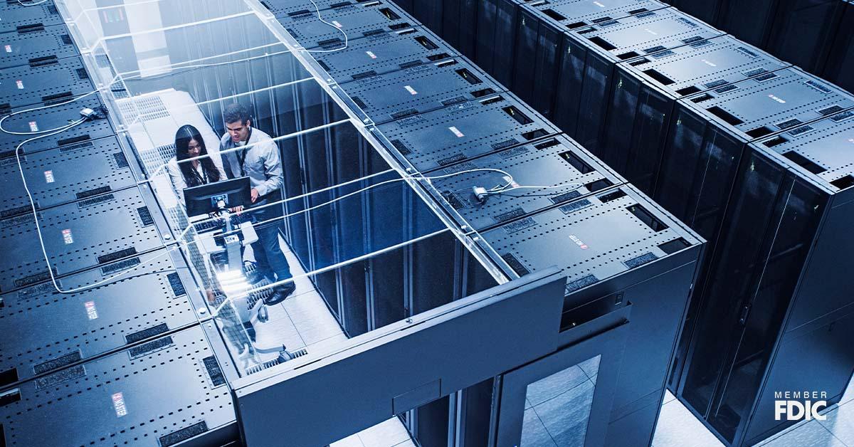 Two tech industry professionals stand in between a row of server racks while analyzing data on a computer.