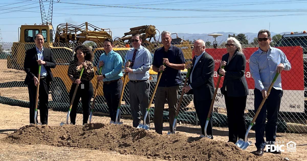 Staff from Cathay Bank and from the Federal Home Loan Bank stand on a gravel pit with shovels with other community professionals in suits.