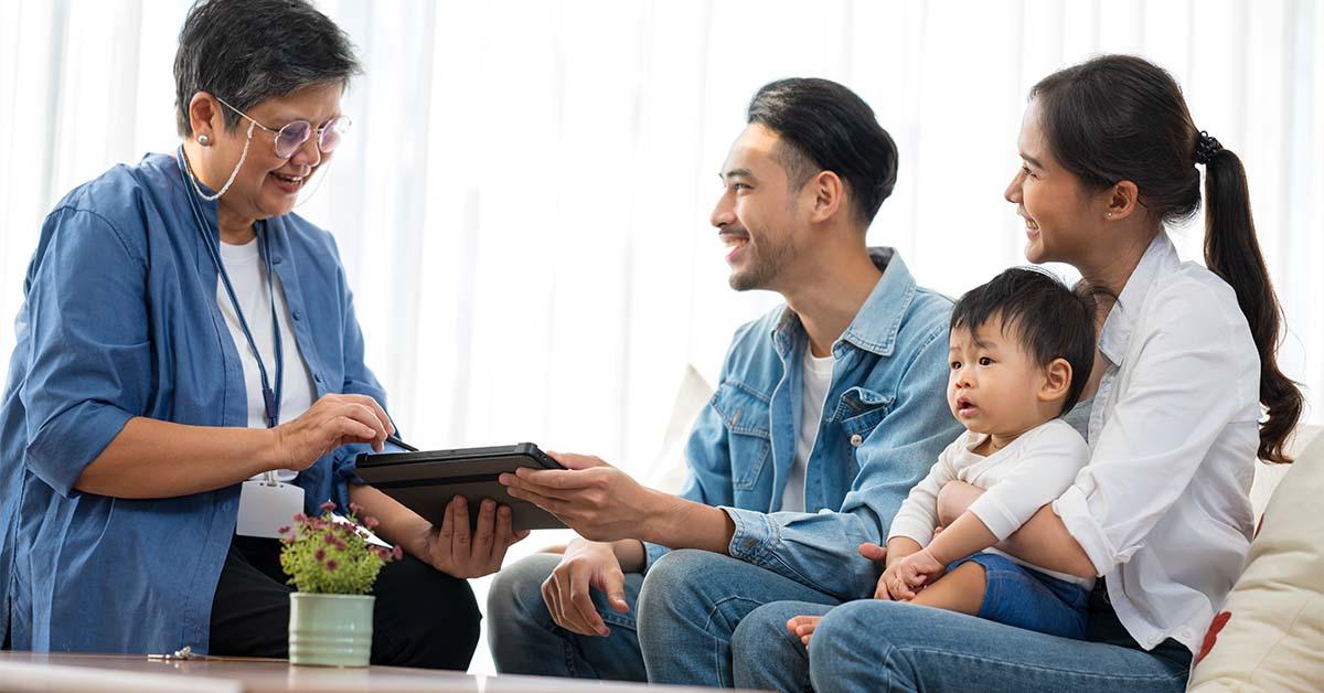 A life insurance policy manager shares a digital device with a family and their child while they sit on a couch in an office. 