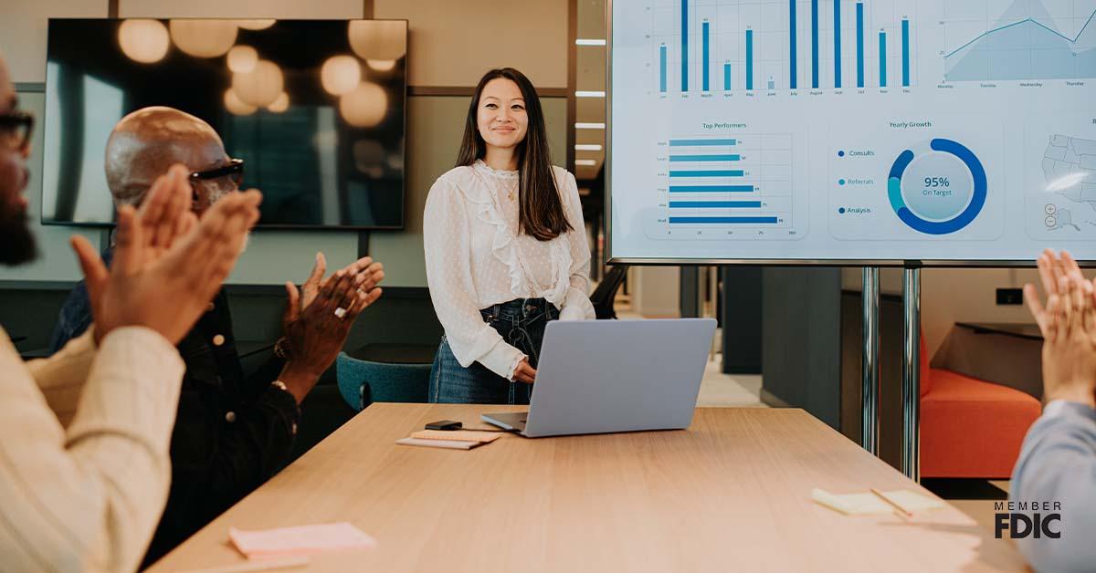 A young woman presents asset-based lending options to a meeting room full of people.