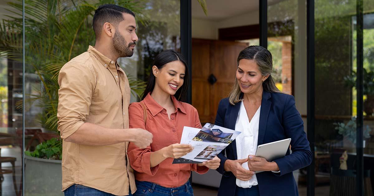 A professional female real estate banker shares purchase options to a female and male couple interested in buying a home while standing in a patio.