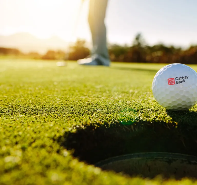 A golf ball with Cathay Bank logo sits outdoors on grass for the annual tournament in California.