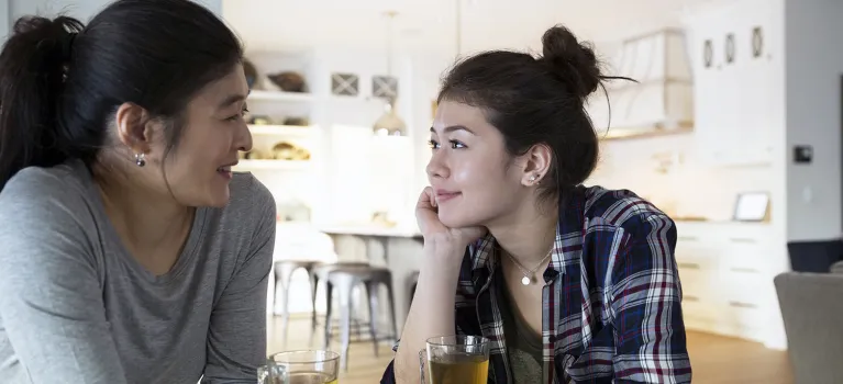 Mother and teenage daughter holding hands drinking tea