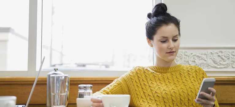 Woman texting and drinking cappuccino in cafe