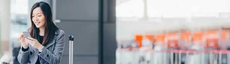 Woman with smartphone and suitcase in airport.