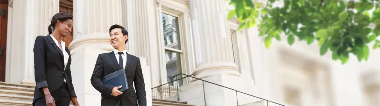 A well dressed man and woman smiling as they as they walk down steps of a courthouse building. 