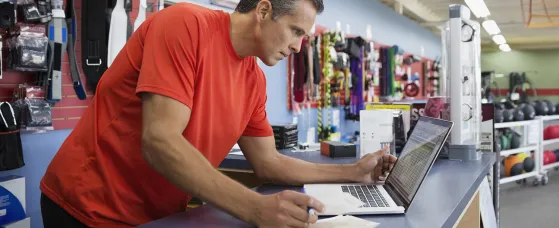 Business owner working at laptop at counter in home gym equipment store