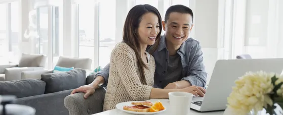 Couple at laptop in kitchen at breakfast