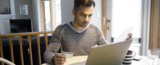 A man with credit card paying bills at laptop